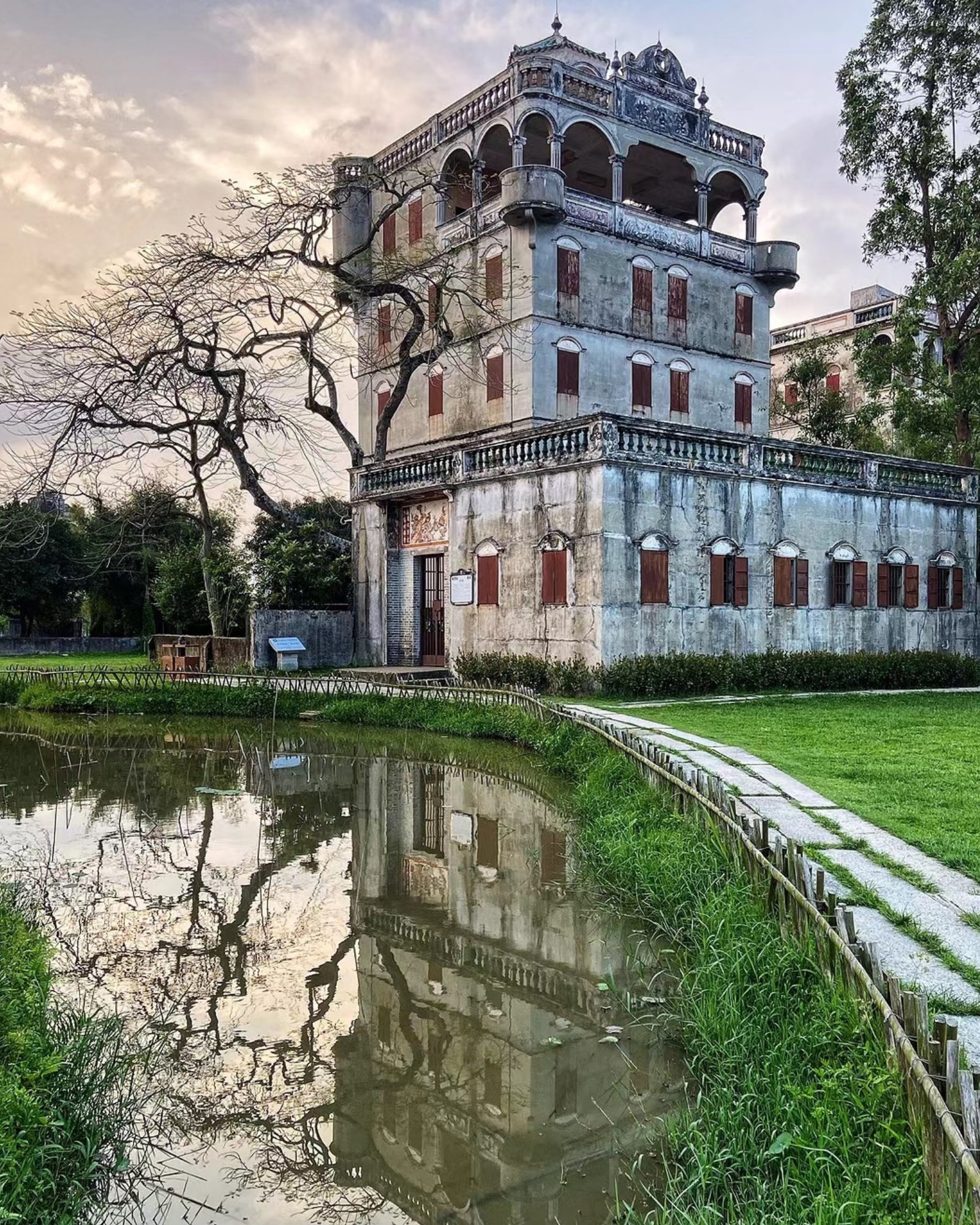 Diaolou building in Zili Village, Kaiping, China, reflected in the nearby pond at sunset.