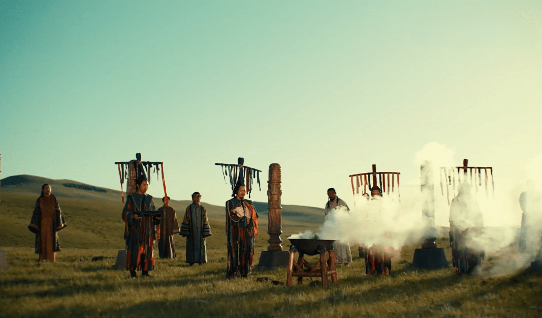 Xianbei people in traditional attire gathered in a misty field, performing a ceremonial ritual with banners and totems in the background.