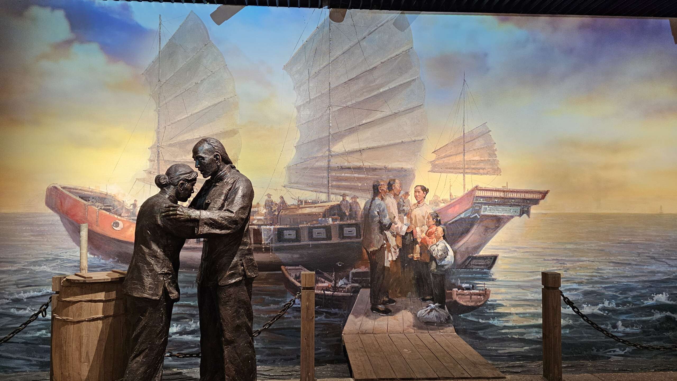 Statues depicting farewell at Guanghai Port with a backdrop of traditional Chinese junks, displayed at Taishan Overseas Chinese Culture Museum.