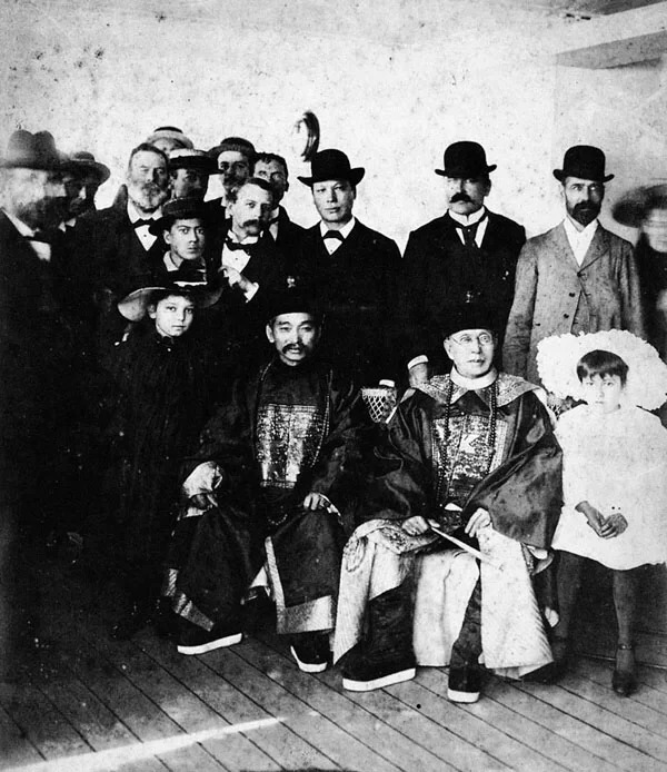 A historical black-and-white photograph of Taishanese diplomats and Chinese community leaders in the 19th century, surrounded by Western officials.