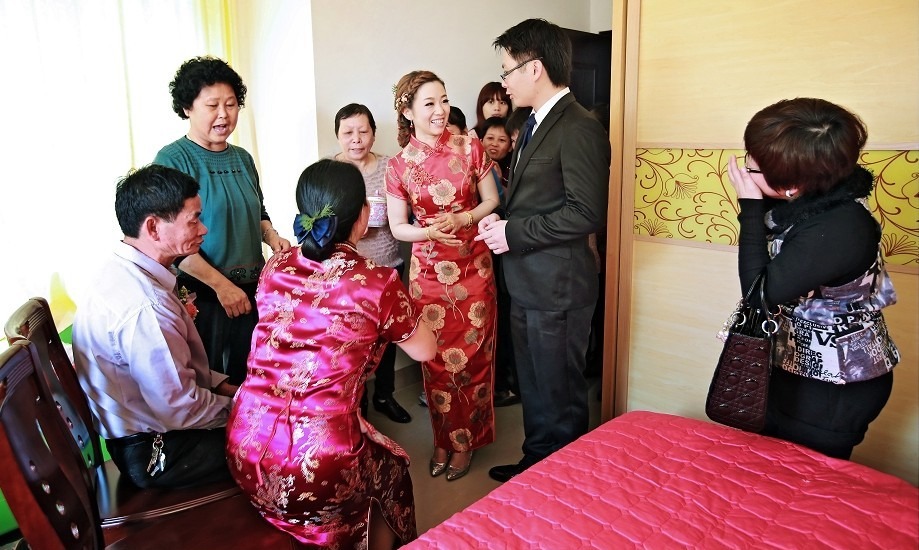 A bride and groom participate in the Jing Cha tea-serving ritual, kneeling before elders in a room with red decor, as part of Guangdong’s marriage traditions.