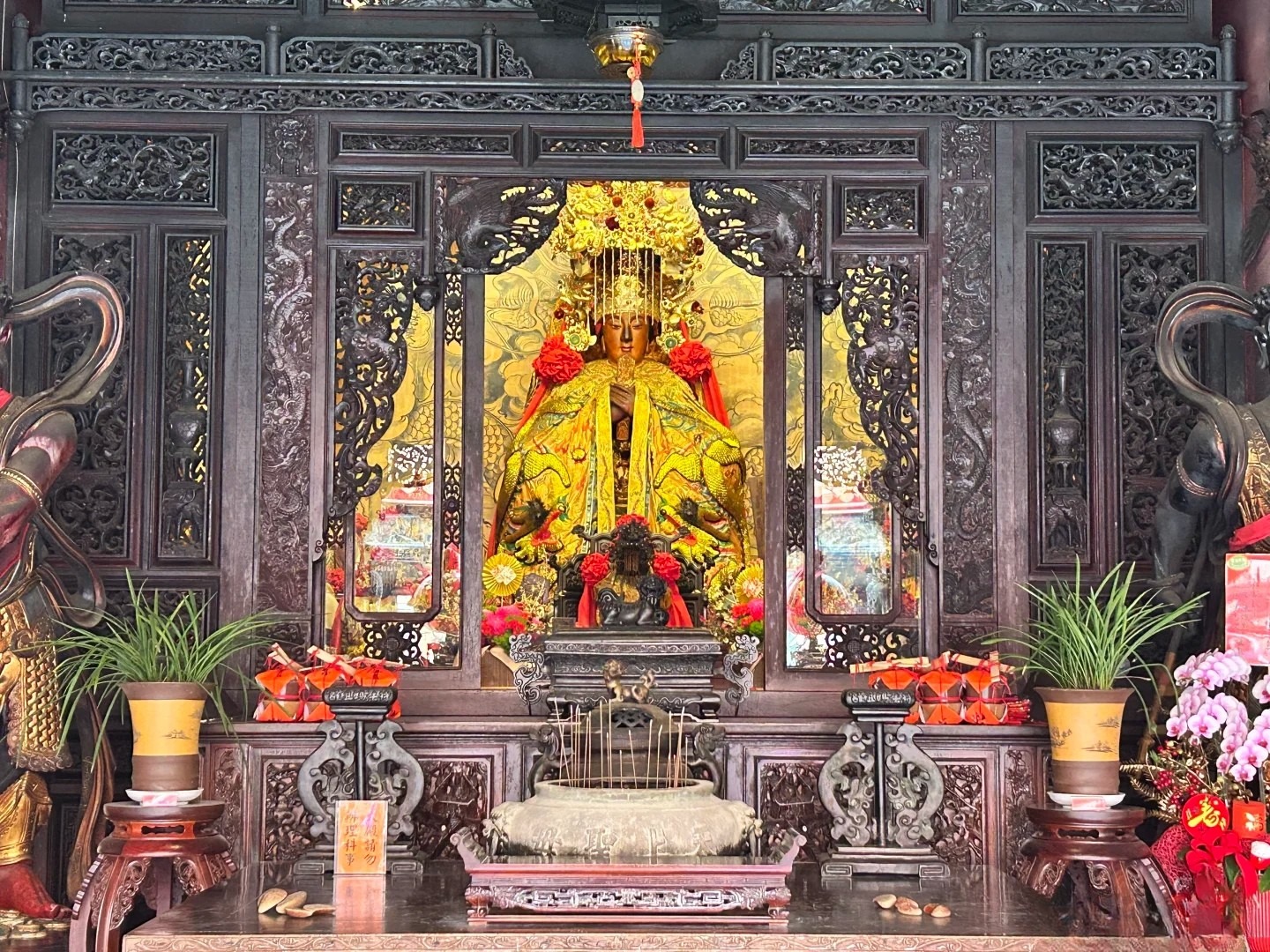 A Mazu statue on an altar in a Chinese ancestral hall, surrounded by offerings and decorations, reflecting Chinese genealogy and spiritual traditions.