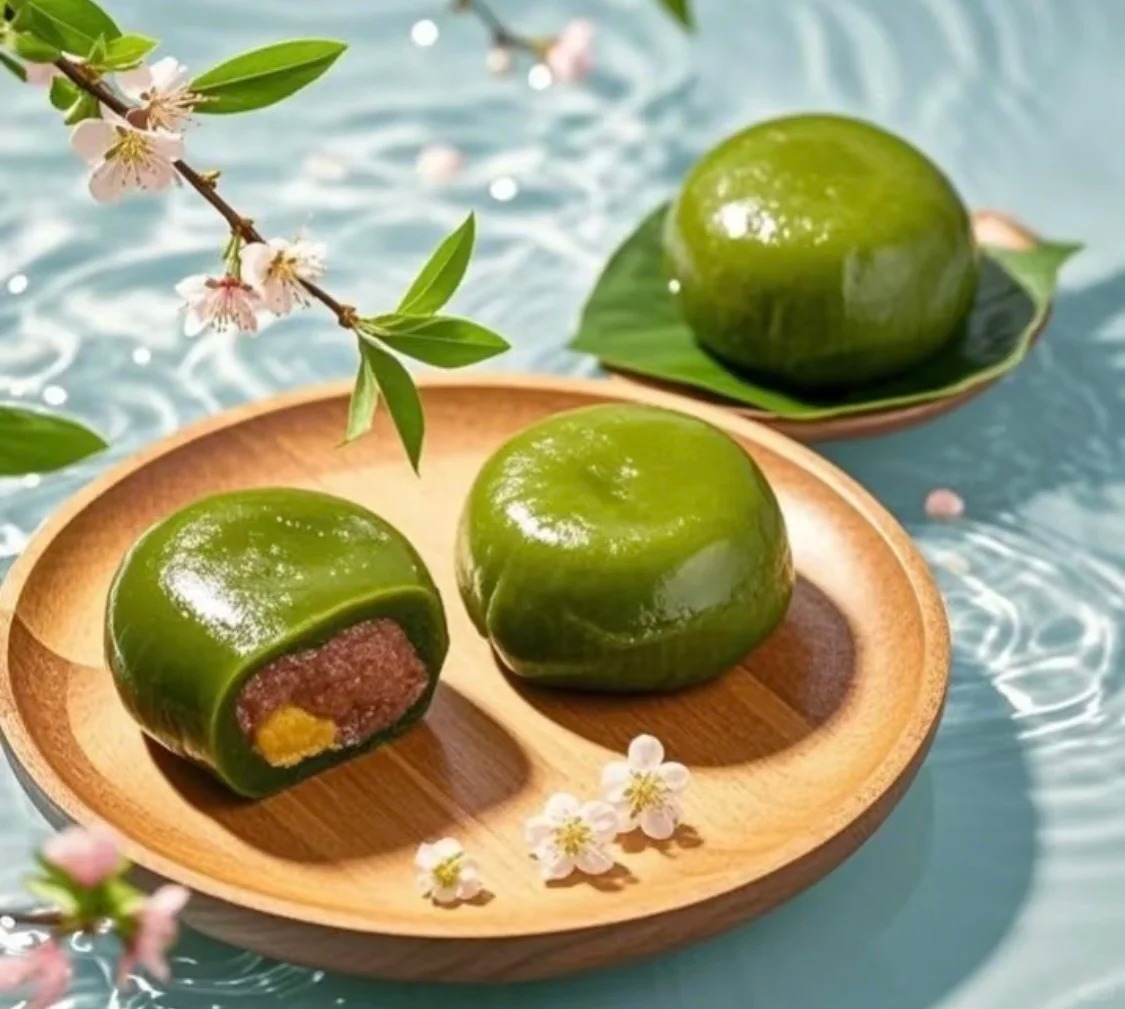 Traditional Qingming qingtuan—vibrant green glutinous rice balls filled with sweet red bean paste, placed on a wooden plate.v