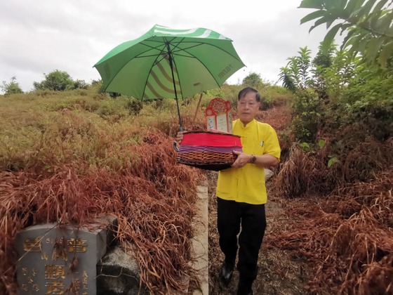 Taoist priest Mr. Wu carrying a basket of offerings under a green umbrella as part of the grave-sweeping ritual.