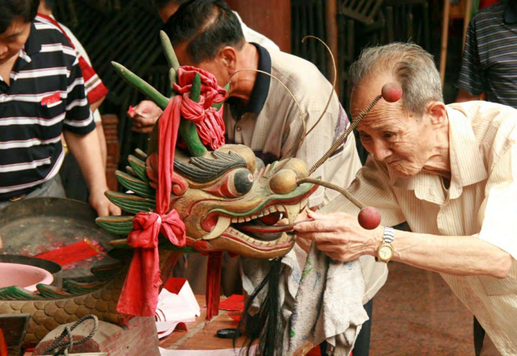 Elder performs dotting-of-the-eyes ritual on dragon head during Dragon Boat Festival preparation, symbolizing spiritual awakening.