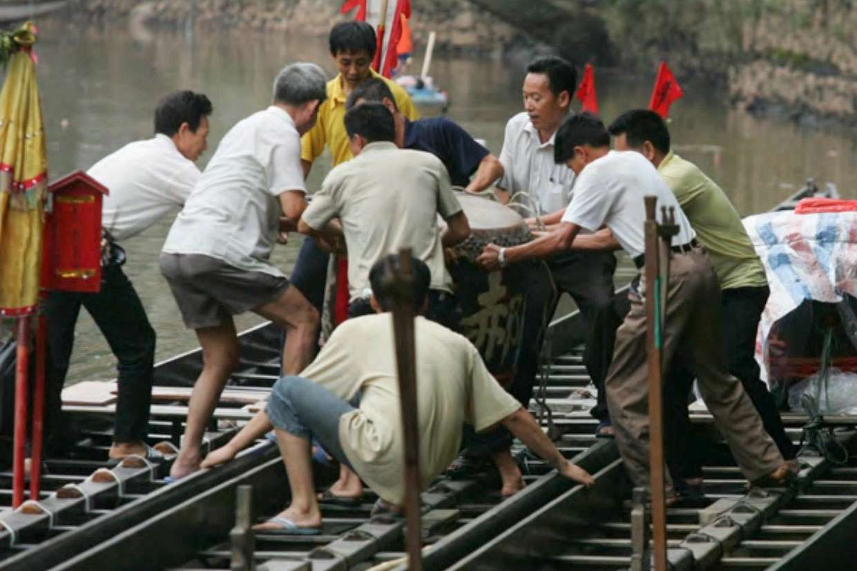 Men lifting and securing the central drum into a dragon boat as part of Dragon Boat Festival preparations.