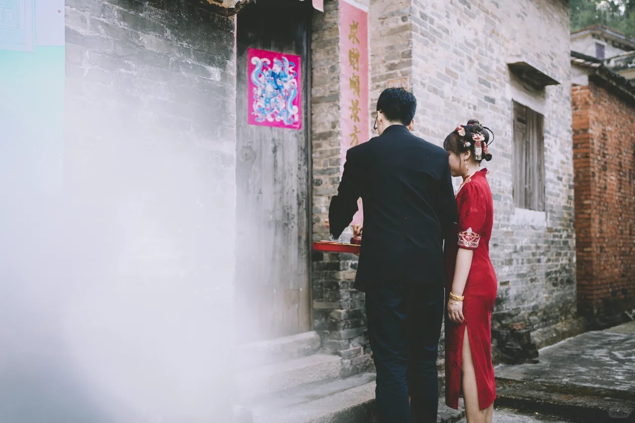 A bride and groom in traditional attire perform a wedding ritual outside a wooden door in a rural village in China.