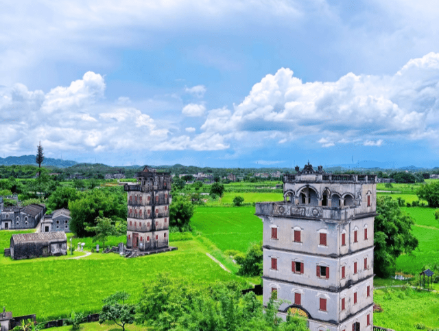 Zilicun Diaolou towers in Kaiping, Guangdong, surrounded by lush green fields under a blue sky.